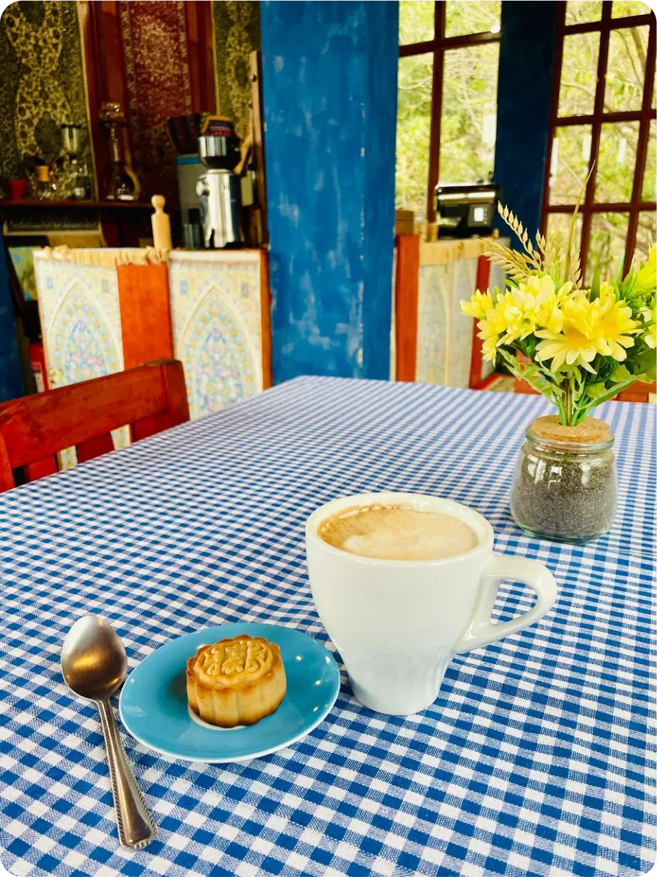A table with a cup of coffee next to a flan dessert decorated with yellow flowers